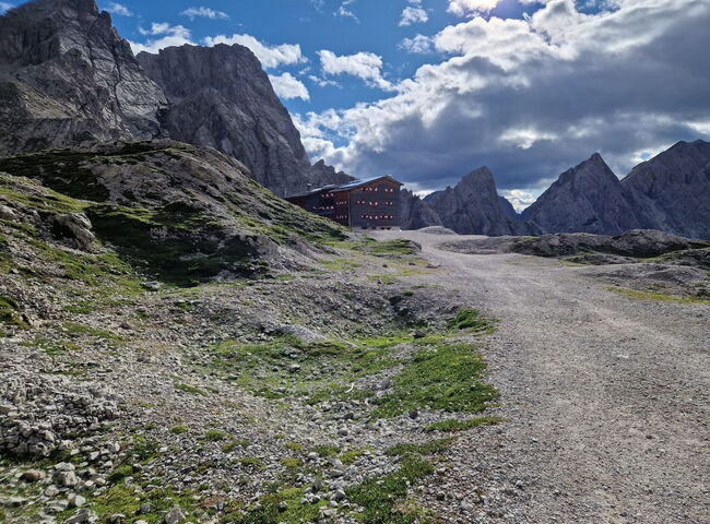 Ein Wanderweg, im Hintergrund die Hütte vor dem Bergpanorama